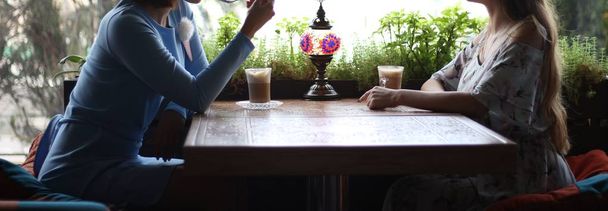 一緒にカフェで楽しんでのガール フレンド。若い女性がコーヒーのカフェで 2 人の女性、café.meeting の会議します。青いドレス、花、彫刻が施されたテーブルの上にはコーヒーと、lamp.communication と交渉のカップ - 写真・画像