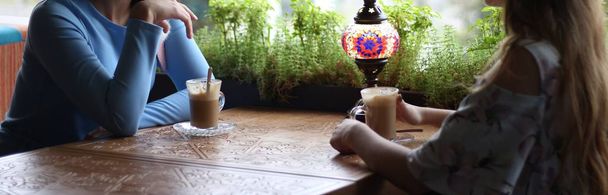 φίλες απολαμβάνοντας τον καφέ μαζί. Νεαρές γυναίκες συνάντηση σε ένα café.meeting δύο γυναικών σε ένα καφενείο για καφέ. μπλε φόρεμα, φόρεμα σε ένα λουλούδι, ένα σκαλιστό τραπέζι είναι ένα φλιτζάνια καφές και μια λάμπα. - Φωτογραφία, εικόνα