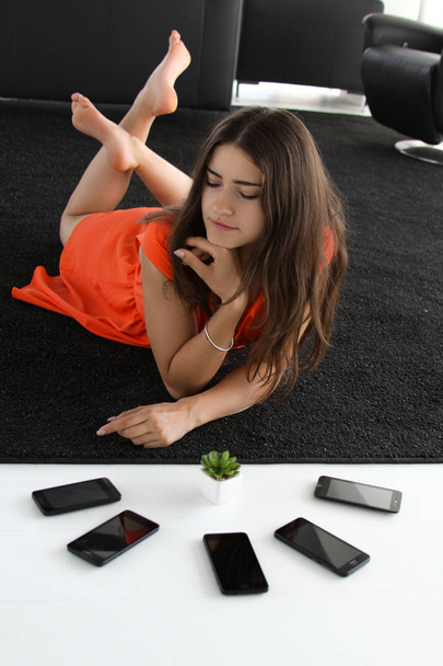 Gorgeous girl in vibrant orange colourful dress laying on the floor with five phones and succulent plant - Photo, Image