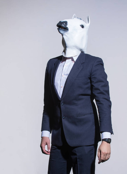 Um homem de fato e uma máscara de cavalo num fundo claro. Conceptual business background
 - Foto, Imagem