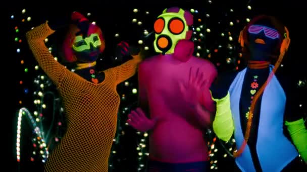 Mujeres sexy y chico en máscara de gas en ropa fluorescente bajo luz negra UV
 - Metraje, vídeo