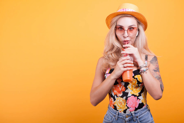 Mujer joven con cabello rubio bebiendo jugo de naranja con gafas de sol
 - Foto, imagen