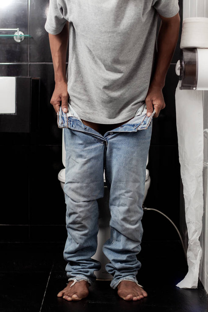 Young man is removing jeans in the bathroom. - Fotografie, Obrázek