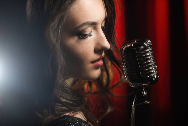 Portrait of beautiful woman singing in microphone on black and red background - Foto, afbeelding