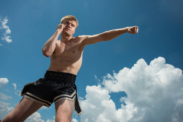 Muscular male fighter training on sky backround. Boxer trains in the open air - 写真・画像