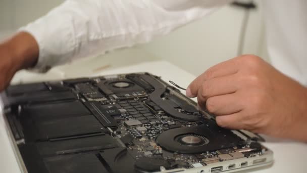 Egy férfi épp egy laptopot javít. A számítógépes javítás fogalma. Közelkép az ember javítás laptop alaplap egy csavarhúzóval. Az alaplap hardverének karbantartása. Lemeztartó, számítógép-javítás - Felvétel, videó