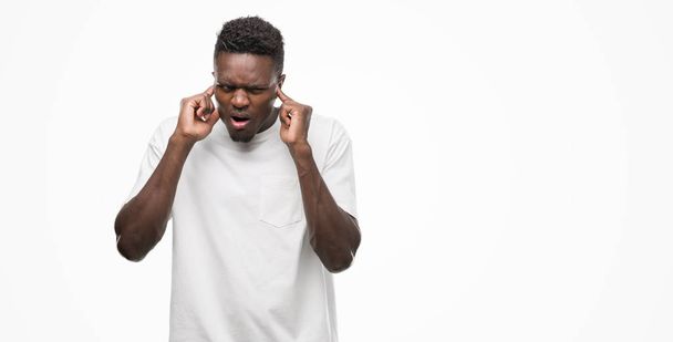 Young african american man wearing white t-shirt covering ears with fingers with annoyed expression for the noise of loud music. Deaf concept. - Foto, immagini
