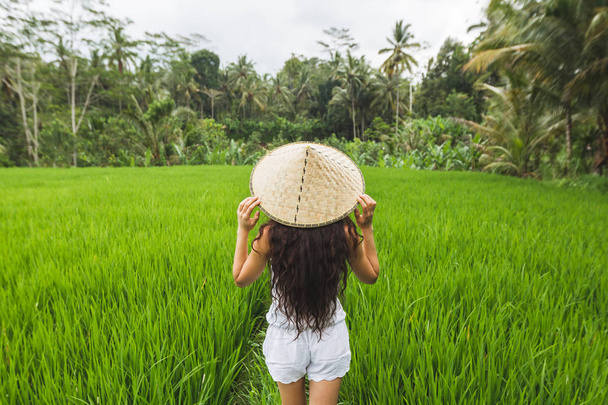 Morena mujer europea posando en campos de arroz con sombrero de paja balinés tradicional
. - Foto, imagen