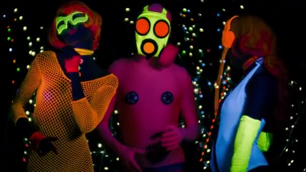 Mujeres sexy y chico en máscara de gas en ropa fluorescente bajo luz negra UV
 - Imágenes, Vídeo