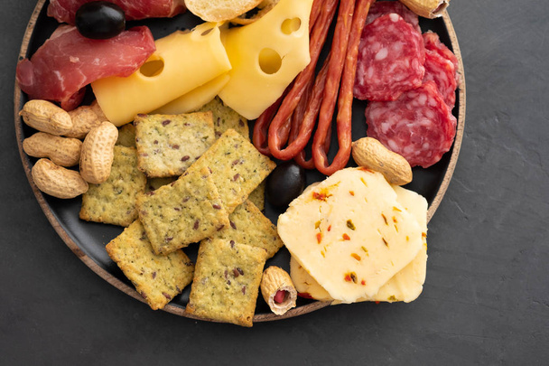 Meat and cheese plate.Traditional italian antipasto, cutting board with salami, cold smoked meat, prosciutto, ham, cheeses, olives, capers on black background. Cheese and meat appetizer. Top view. - Photo, Image