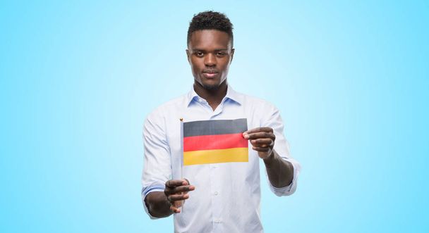 Young african american man holding german flag with a confident expression on smart face thinking serious - Foto, Imagem