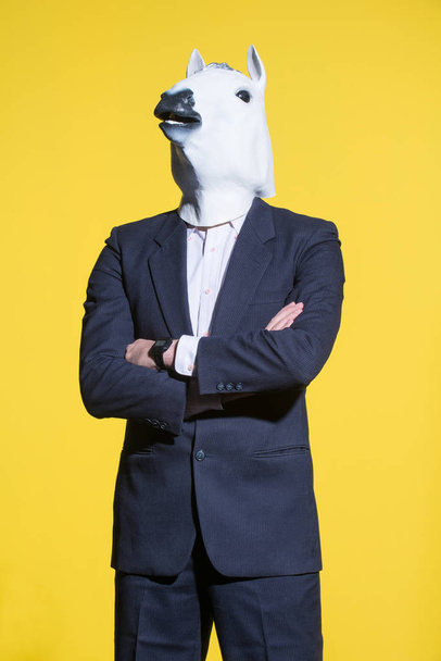 Un hombre con traje y una máscara de caballo sobre un fondo amarillo. Contexto empresarial conceptual
 - Foto, Imagen