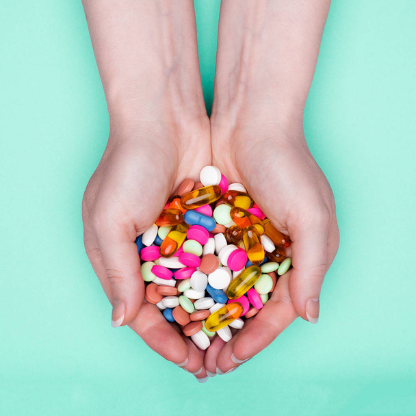 Close up of female hands holding heap of colorful medication pills over pastel blue background. Patient taking medication. - Fotó, kép