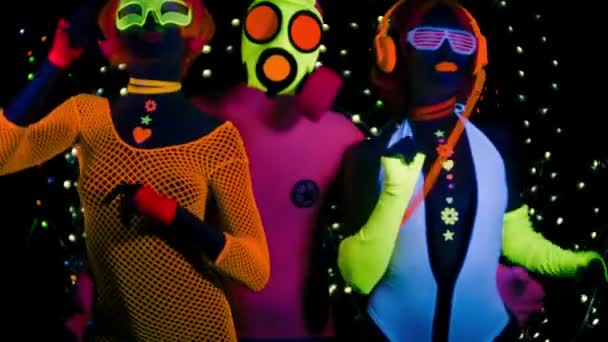 Mujeres sexy y chico en máscara de gas en ropa fluorescente bajo luz negra UV
 - Metraje, vídeo