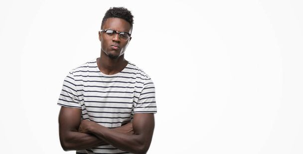 Młody człowiek african american sobie okulary i granatowy t-shirt sceptykiem i nerwowy, dezaprobaty wyrażenie na twarz z skrzyżowanymi rękami. Negatywne osoba. - Zdjęcie, obraz
