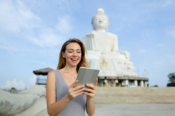 Młoda dziewczyna Europejskiej za pomocą tabletu w pobliżu biały posąg Buddy w Phuket. - Zdjęcie, obraz