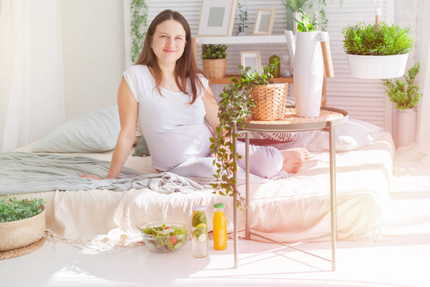 Young pregnant woman posing in light modern scandinavian bedroom interior - Foto, afbeelding