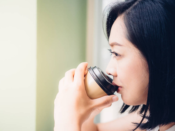 Asian woman drinks hot coffee, relax and enjoy warm morning sunlight. - Photo, image