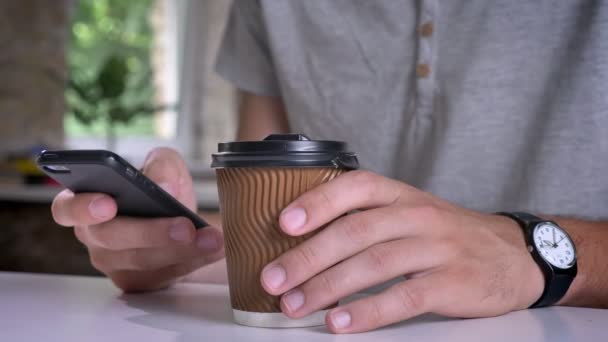 Close shot of mans hands holding coffee and typing on phone in office - Imágenes, Vídeo