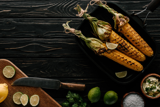 top view of grilled corn, cutting board with lemon and lime slices with knife on wooden table  - Foto, immagini