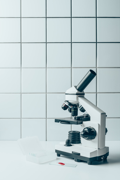 blood sample and optical microscope on white tablet in front of tiled wall - Fotoğraf, Görsel