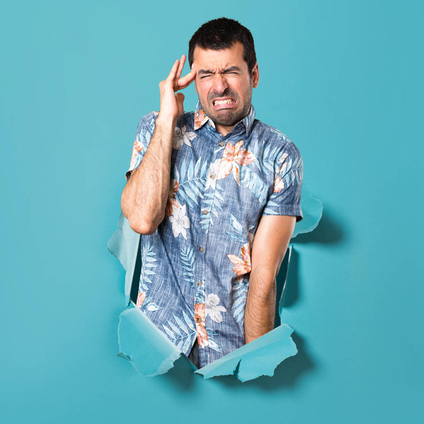 Hombre guapo frustrado con camisa de flores a través de un agujero de papel azul
 - Foto, Imagen