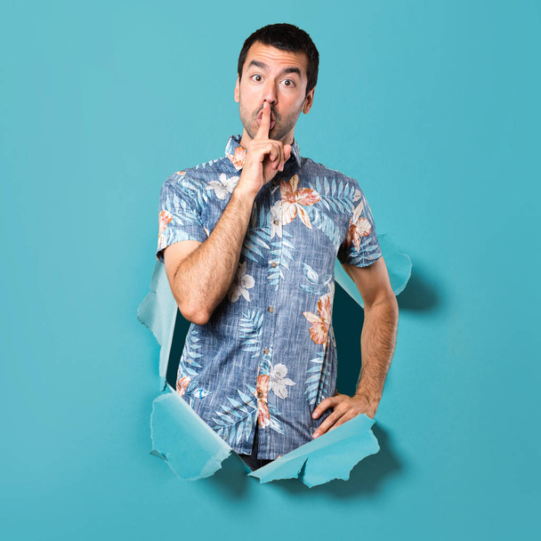 Homem bonito com camisa de flor fazendo gesto de silêncio através de um buraco de papel azul
 - Foto, Imagem