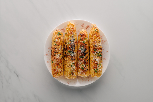 top view of grilled corn with salt and chili spice on plate on marble table  - Foto, afbeelding