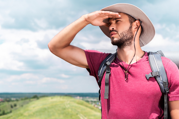 traveler in hat with backpack looking away on summer meadow - Photo, Image