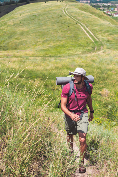 viajero en sombrero con mochila y alfombra turística caminando por el camino
 - Foto, imagen