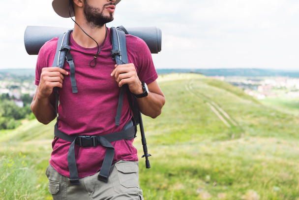 Ausgeschnittene Ansicht eines Reisenden mit Rucksack und Touristenmatte beim Spazierengehen auf der Wiese - Foto, Bild