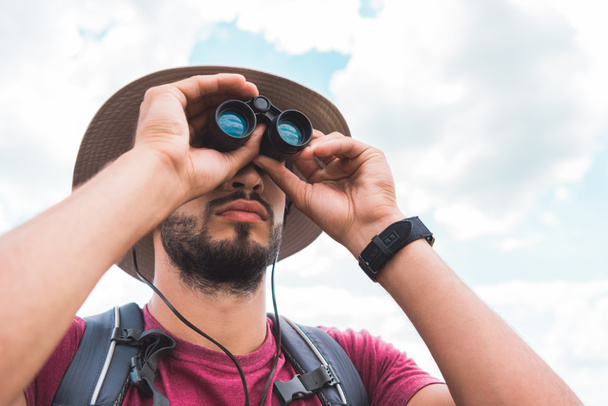 handsome male tourist in hat looking in binoculars - Photo, Image