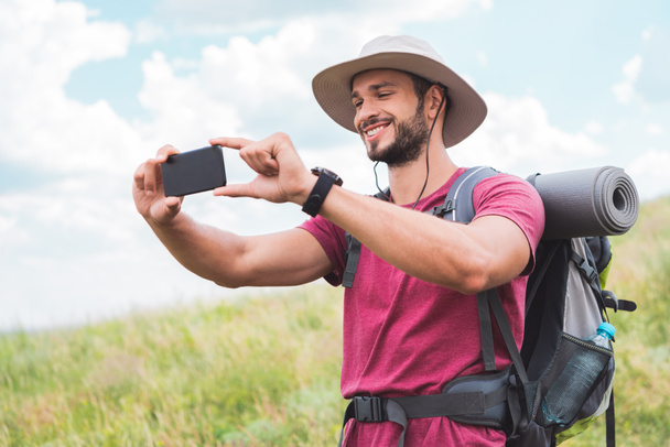 traveler with backpack taking photo on smartphone on summer meadow - Foto, Imagem