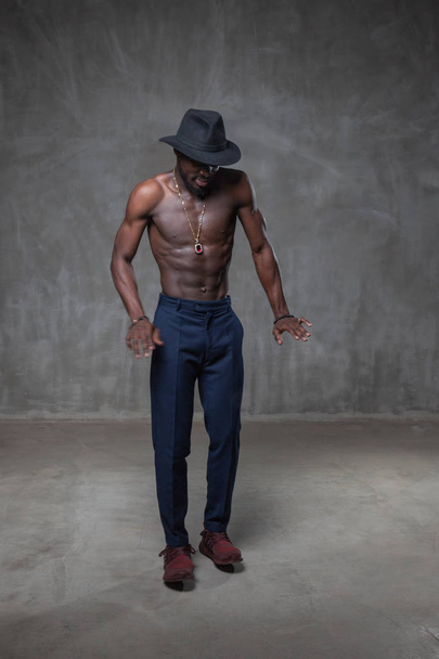 strong African American young man in black hat dancing against grunge concrete background - 写真・画像