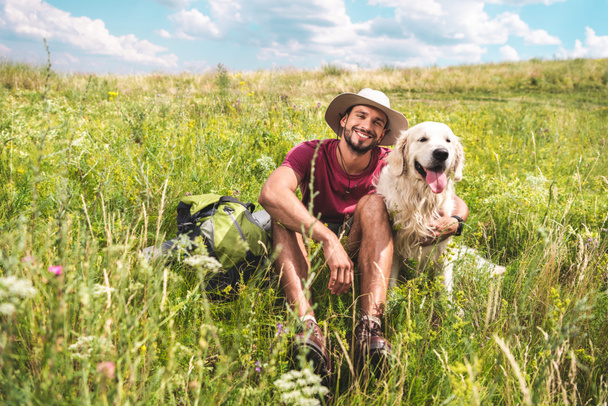 male traveler sitting with dog on green summer meadow - Foto, imagen