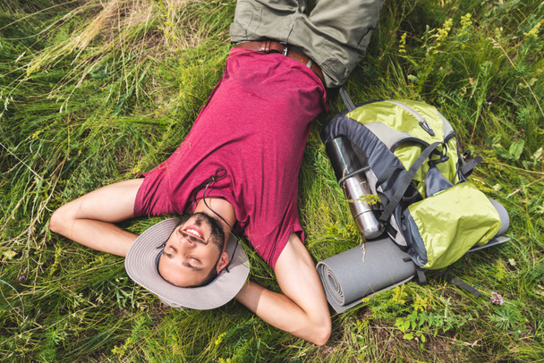 pohled shora mladých turistů s odpočinkem na trávě s batohem, turistické mat a termosky - Fotografie, Obrázek