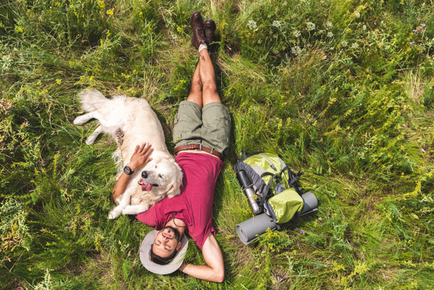 top view of tourist and golden retriever dog lying on green grass with backpack - Фото, зображення