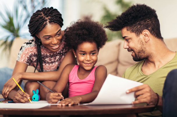 Maman et papa dessinent avec leur fille. Famille afro-américaine passer du temps ensemble à la maison
. - Photo, image