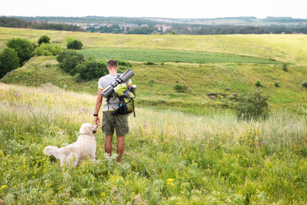 вид сзади путешественника с рюкзаком прогулки с собакой на летнем лугу
 - Фото, изображение
