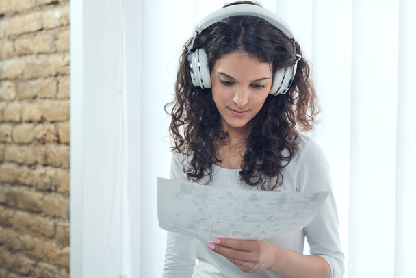 Mladá žena poslouchat hudbu během čtení něco ve své kanceláři - Fotografie, Obrázek