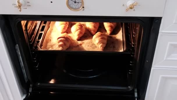 Vrouwelijke kok bakken croissants in witte oven in de keuken - Video