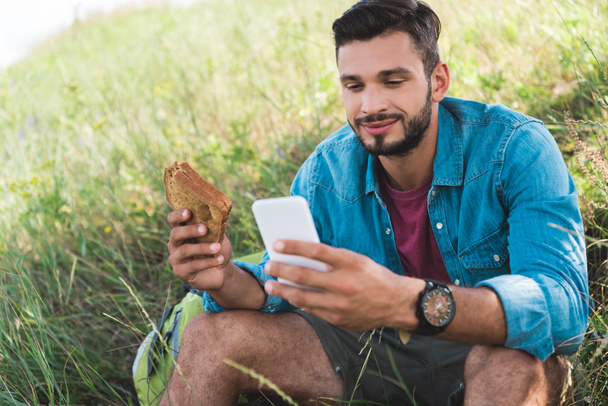 voyageur utilisant smartphone et manger un sandwich sur la prairie d'été
 - Photo, image