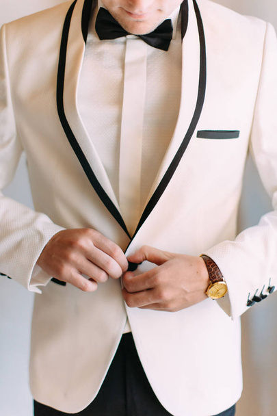 Tha hands of the groom buttoning the suit jacket. - Zdjęcie, obraz
