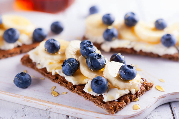 Healthy sandwiches with berry, fruit, honey and cream cheese on white wooden boar - 写真・画像