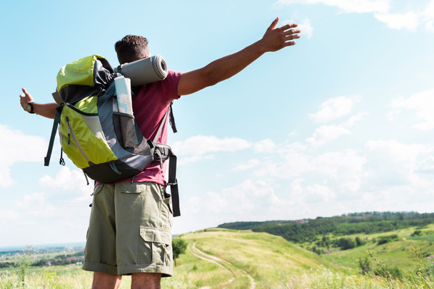 touriste avec sac à dos debout avec les mains tendues sur la prairie d'été avec ciel nuageux
 - Photo, image