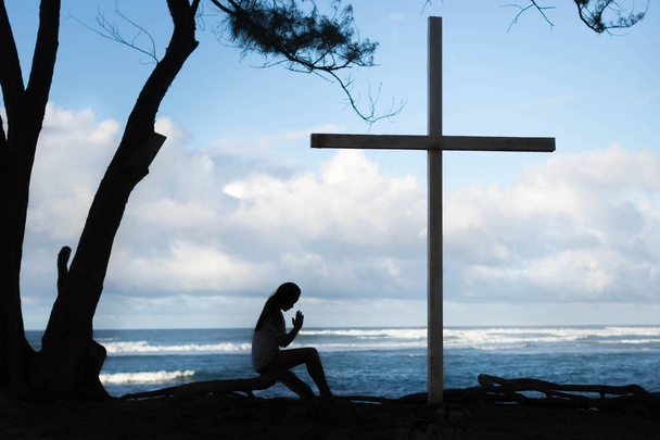 Silhouette of girl praying to large cross. Ocean background - Photo, Image