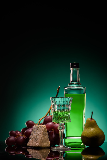 close-up shot of absinthe with fresh pear, grapes and cheese on mirror surface on dark blue background - Foto, afbeelding