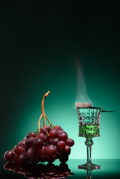 glass of burning absinthe with sugar and grapes on dark blue background - Фото, зображення