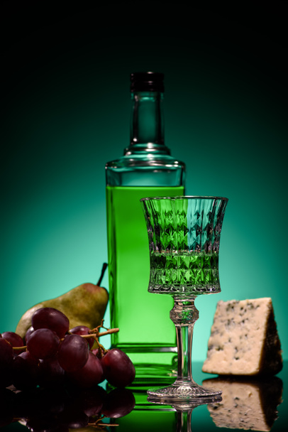 close-up shot of absinthe with fruits and cheese on mirror surface on dark blue background - Фото, изображение