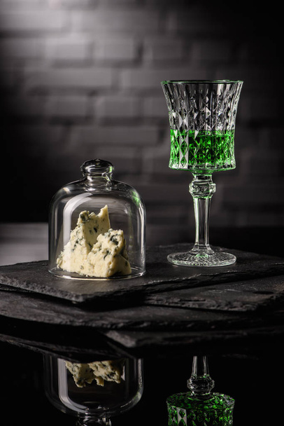 Close-up shot van glas van absint met een plakje kaas op donkere bakstenen muur achtergrond - Foto, afbeelding